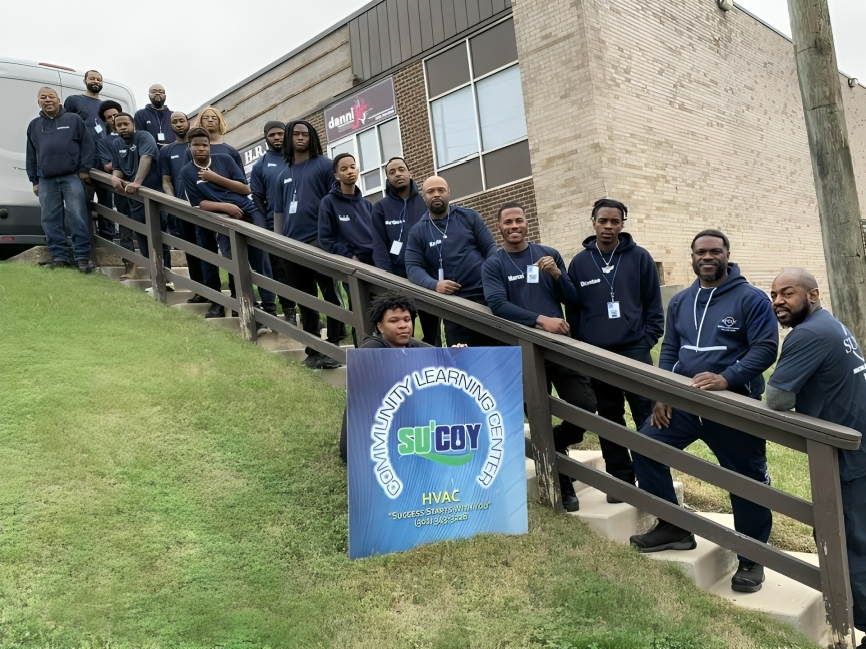 Group of HVAC trainees at the Sucoy Community Learning Center in Washington, DC, posing on steps with a Sucoy HVAC sign.